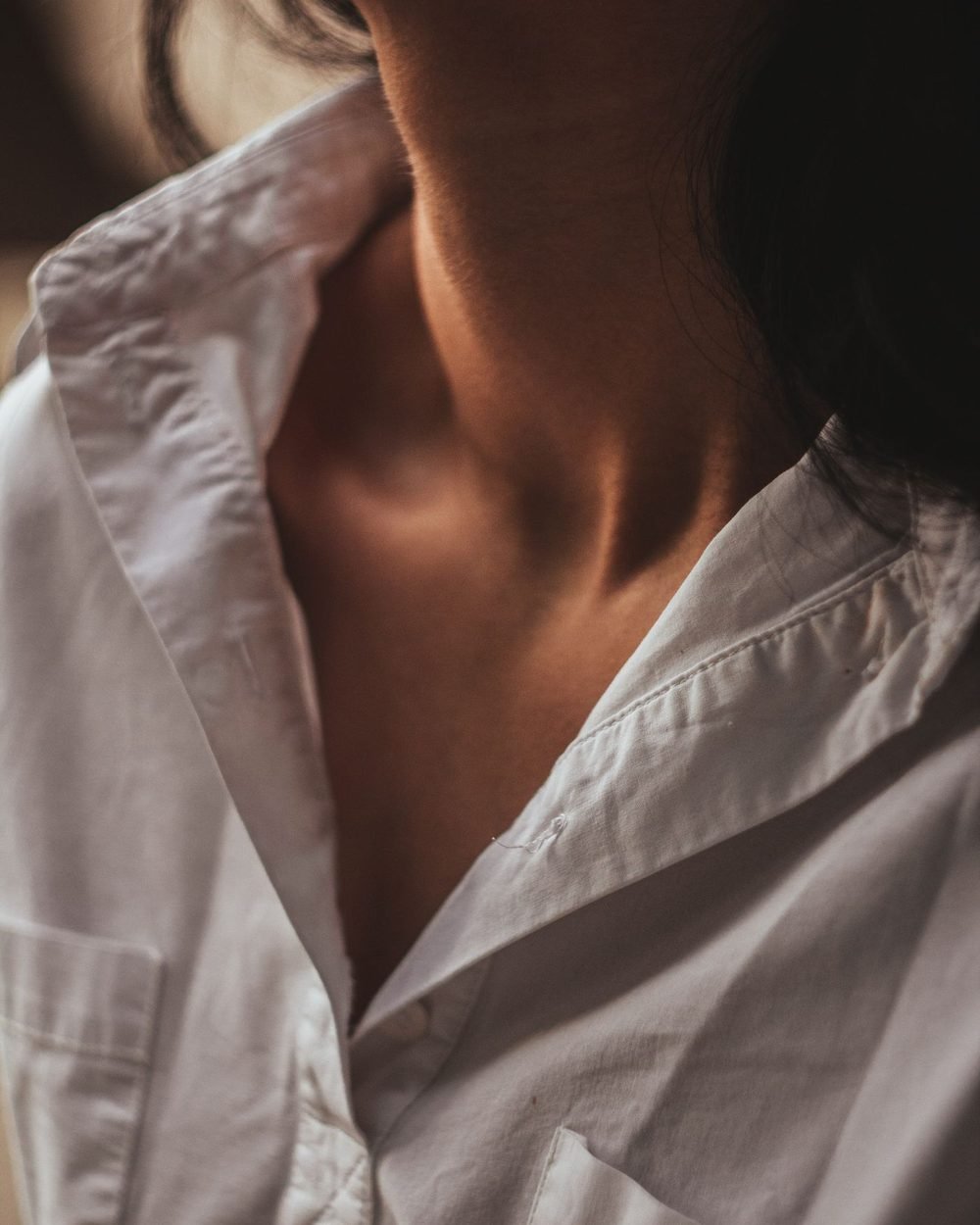 Close-up of a crisp white cotton shirt collar and chest pocket in warm light.