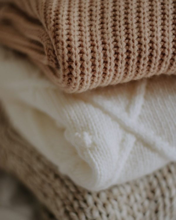 Folded cream and oatmeal knitwear stacked in soft daylight.