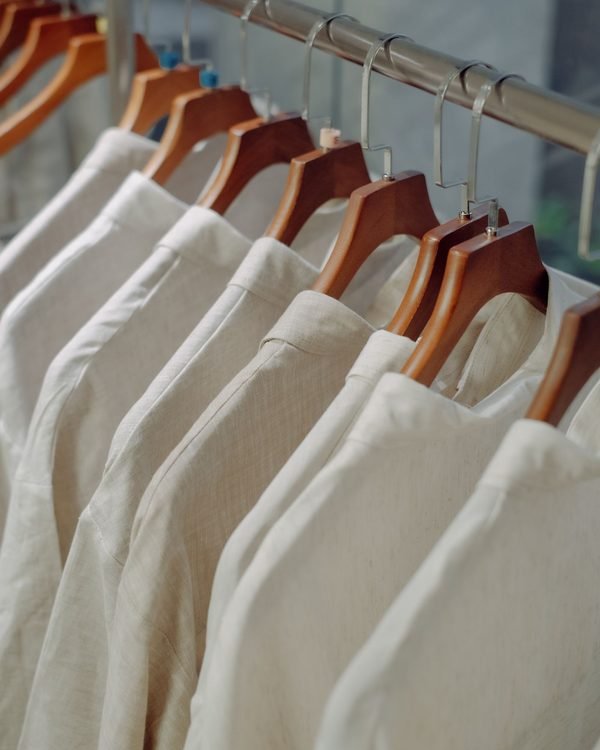 A rail of cream and natural linen shirts on wooden hangers.