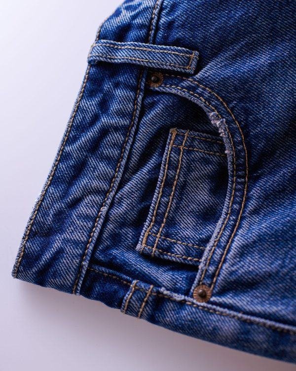 Close-up of indigo denim showing copper rivets and contrast topstitching.